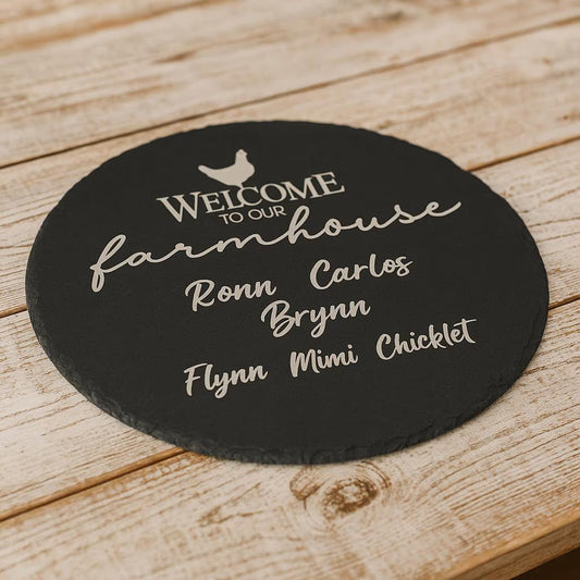 Round black slate coaster with 'Welcome to our farmhouse' text on a wooden surface