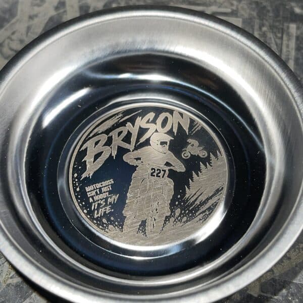 Close-up of a metal circular badge showing the word 'BRYSON' with a motocross rider illustration, the number 227, and the slogan 'Motocross isn’t just a hobby—it’s my life.'