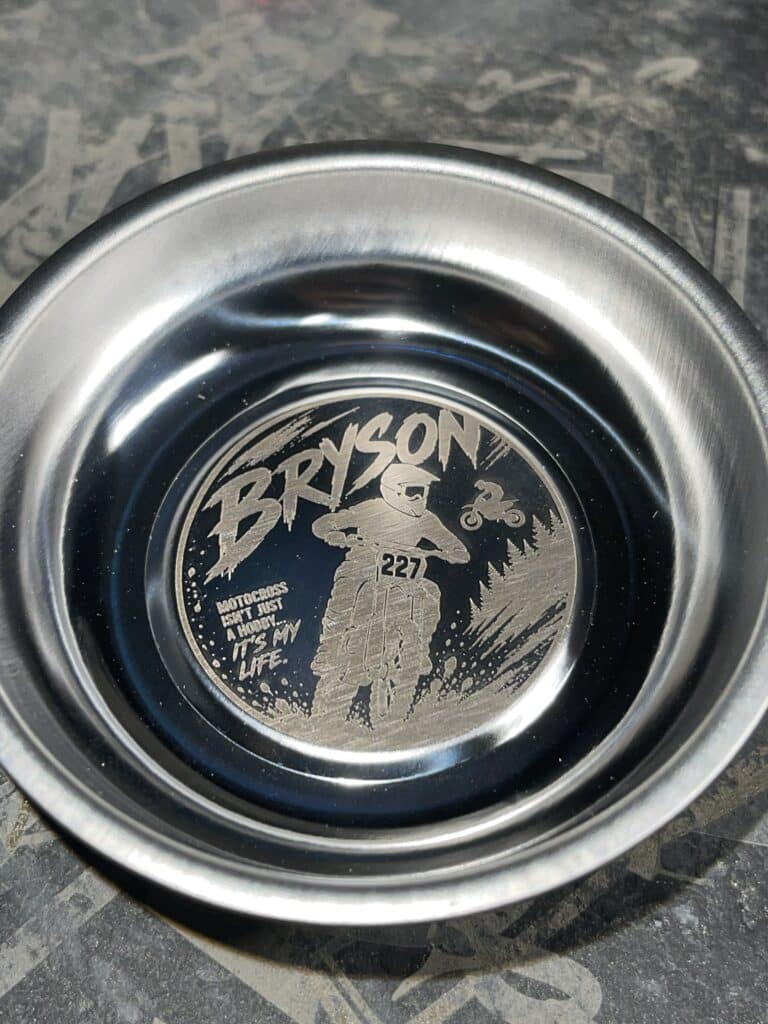 Close-up of a metal circular badge showing the word 'BRYSON' with a motocross rider illustration, the number 227, and the slogan 'Motocross isn’t just a hobby—it’s my life.'