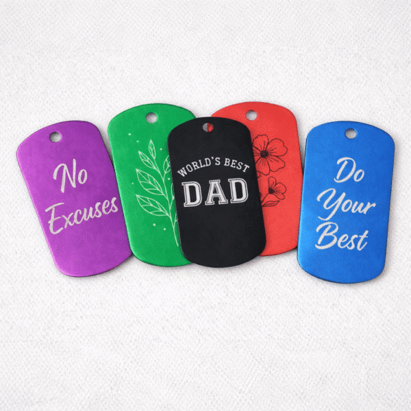 Five Engraved Dog Tags with Optional Chain are shown on a white background, featuring messages like “No Excuses,” “Do Your Best,” “WORLDS BEST DAD,” and designs with leaves and flowers.