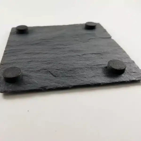 A Custom Laser Engraved Slate Coaster, square and black with four round rubber feet at each corner, displayed on a white background.