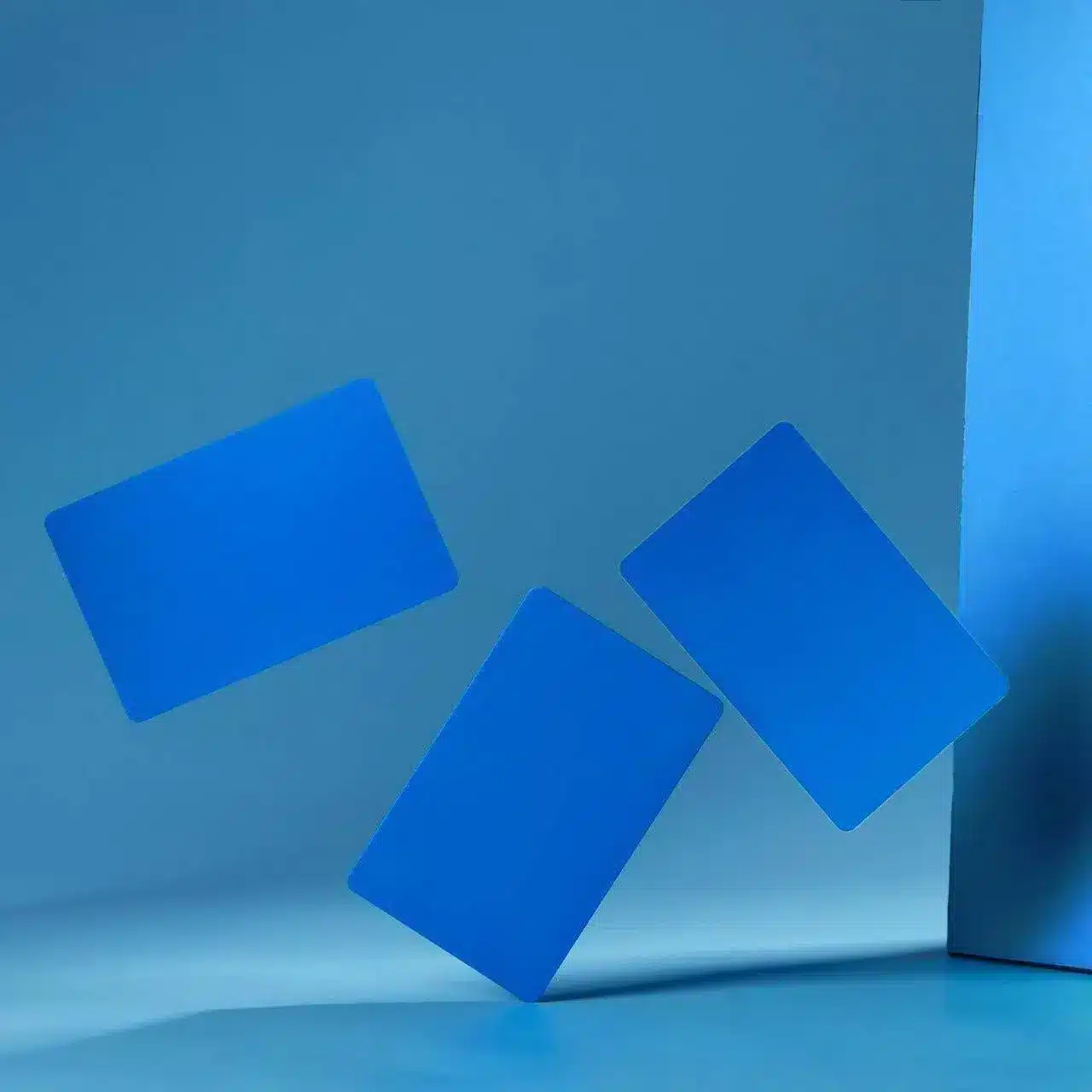 Three .8mm Engraved Aluminum Business Cards in solid blue appear to be floating or falling in midair against a plain blue background.