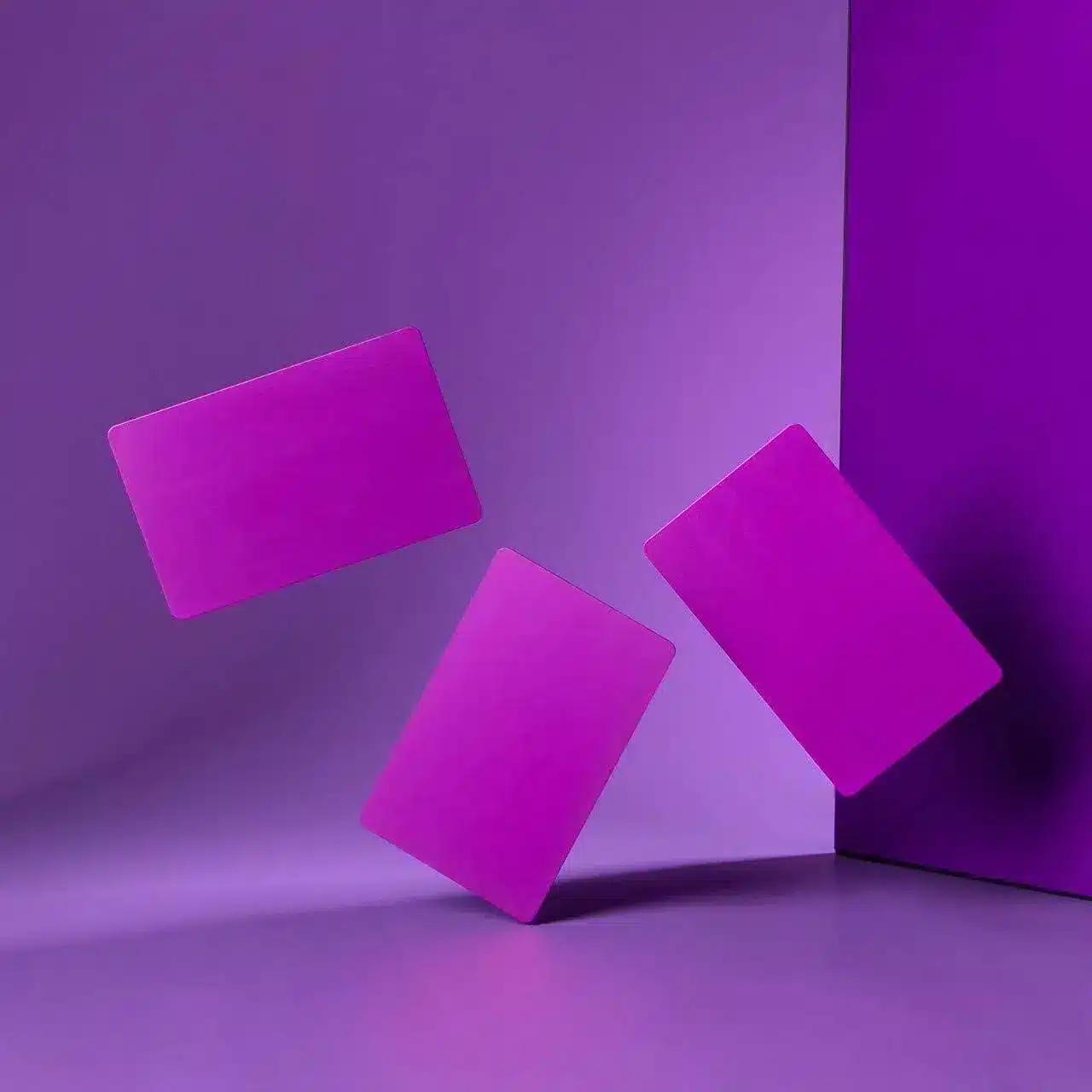 Three vibrant .8mm Engraved Aluminum Business Cards in purple appear to float against a matching background, casting soft shadows and adding a dynamic, surreal touch.
