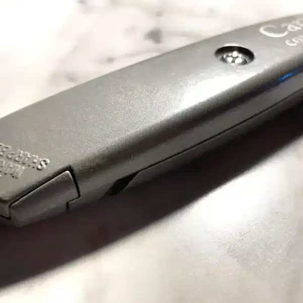 A close-up of the Engraved Safety Utility Knife, featuring a gray finish and retractable blade, rests angled on a marbled surface with "Catre" and "Contractor" labels visible, showing its blade storage compartment.