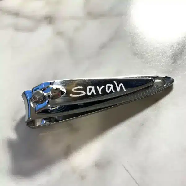 An Engraved Mini Nail Clipper personalized with the name Sarah sits on a light marble surface.