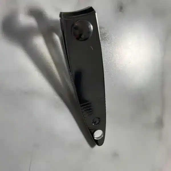 An Engraved Mini Nail Clipper rests closed on a white marble surface, casting a shadow to the left.