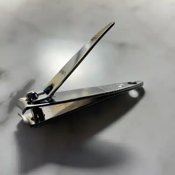The Engraved Mini Nail Clipper is open and resting on a light gray marble surface, casting a faint shadow.
