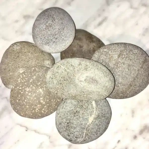 Seven smooth, round 1-5" Aged Rustic Engraved River Rocks in gray and beige are arranged on a white marbled surface.