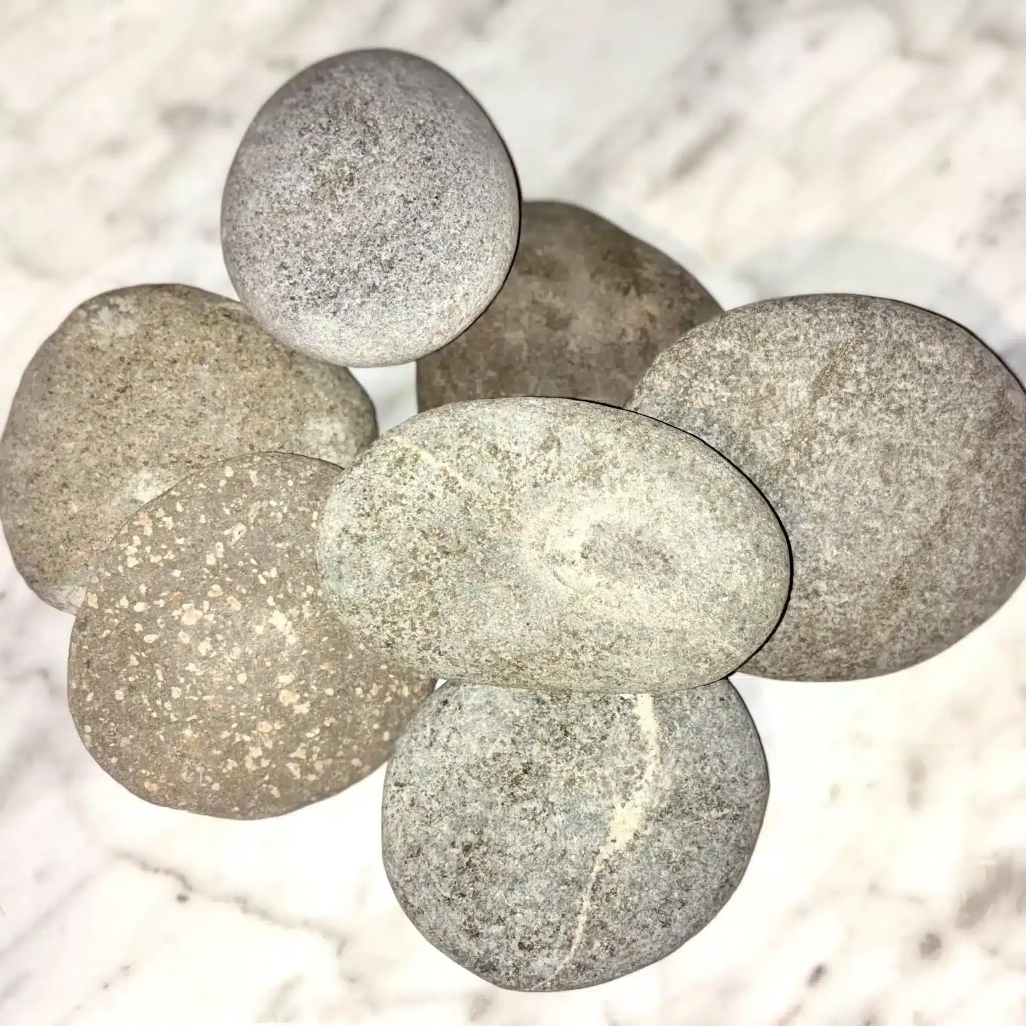 Seven smooth, round 1-5" Aged Rustic Engraved River Rocks in gray and beige are arranged on a white marbled surface.