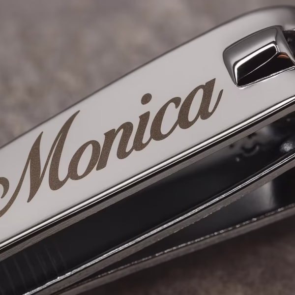 A close-up of Standard Stainless Steel Nail Clippers engraved with the name Monica in elegant script on their shiny surface, set against a blurred gray background.