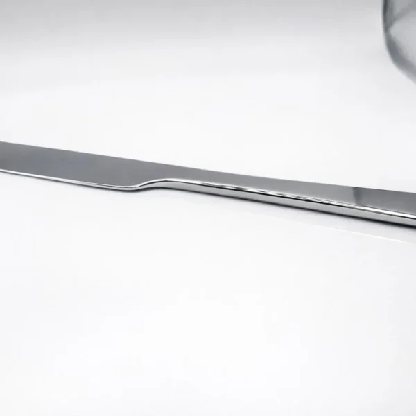 A Premium 9.5 Inch Personalized Butter Knife with a sleek, modern design rests on a white surface, with part of a glass visible in the corner.