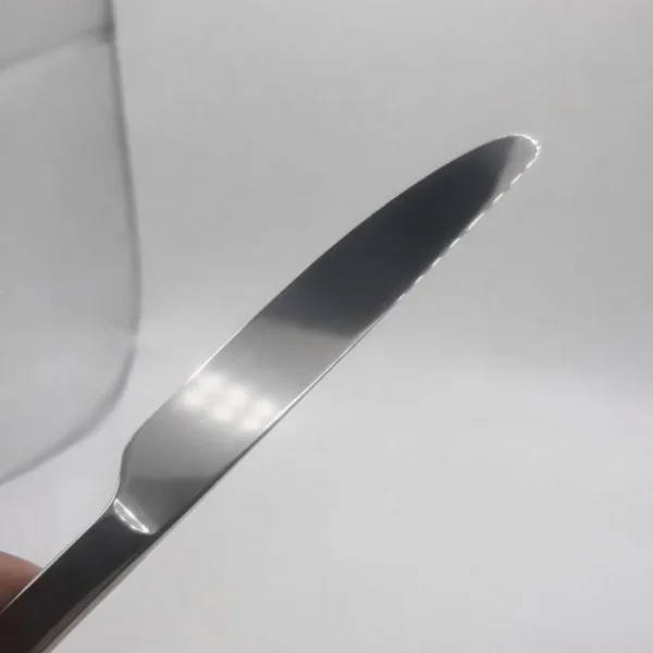 A close-up of the Premium 9.5 Inch Personalized Butter Knife, stainless steel, held at an angle against a plain white background, with a slightly blurred glass object visible in the corner.