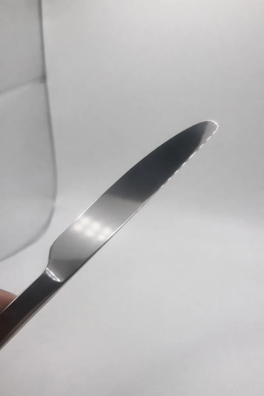 A close-up of the Premium 9.5 Inch Personalized Butter Knife, stainless steel, held at an angle against a plain white background, with a slightly blurred glass object visible in the corner.