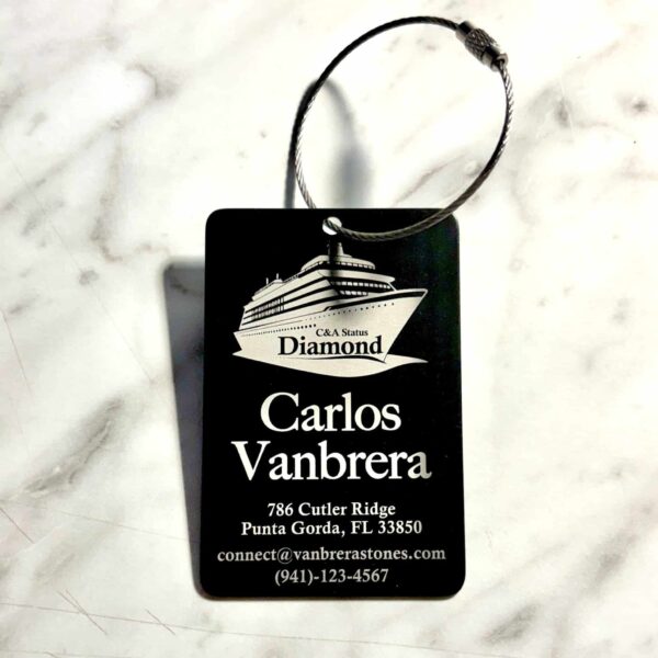 A Personalized Custom Engraved Metal Luggage Tag, black with a cruise ship graphic, “C&A Status Diamond,” Carlos Vanbrera’s info, and chain, is shown on a white surface.