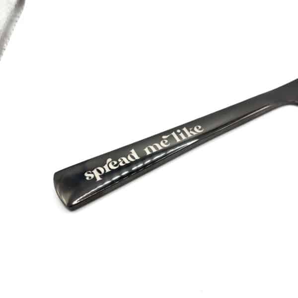 A close-up of the 9" Custom Engraved Black Knife handle with "spread me" playfully engraved in lowercase letters, shown against a white background.