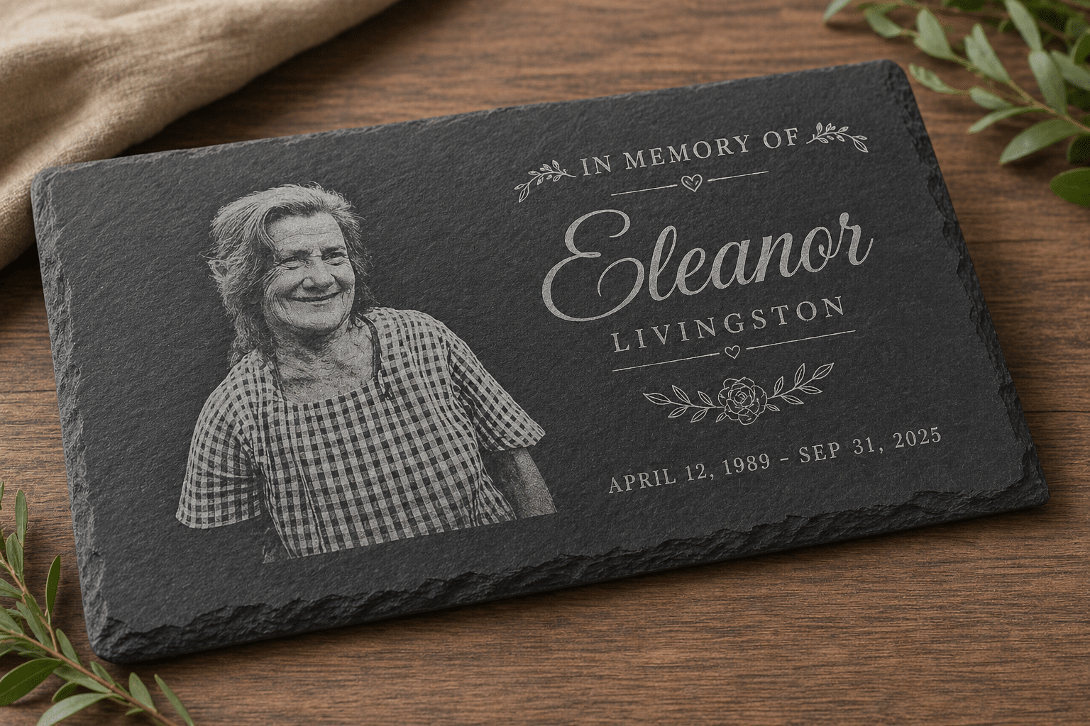 The Engraved Slate Plaque | Rectangular Sign displays a smiling woman, floral accents, and the inscription: In Memory of Eleanor Livingston, April 12, 1989 – Sep 31, 2025. It is placed on a wooden surface.