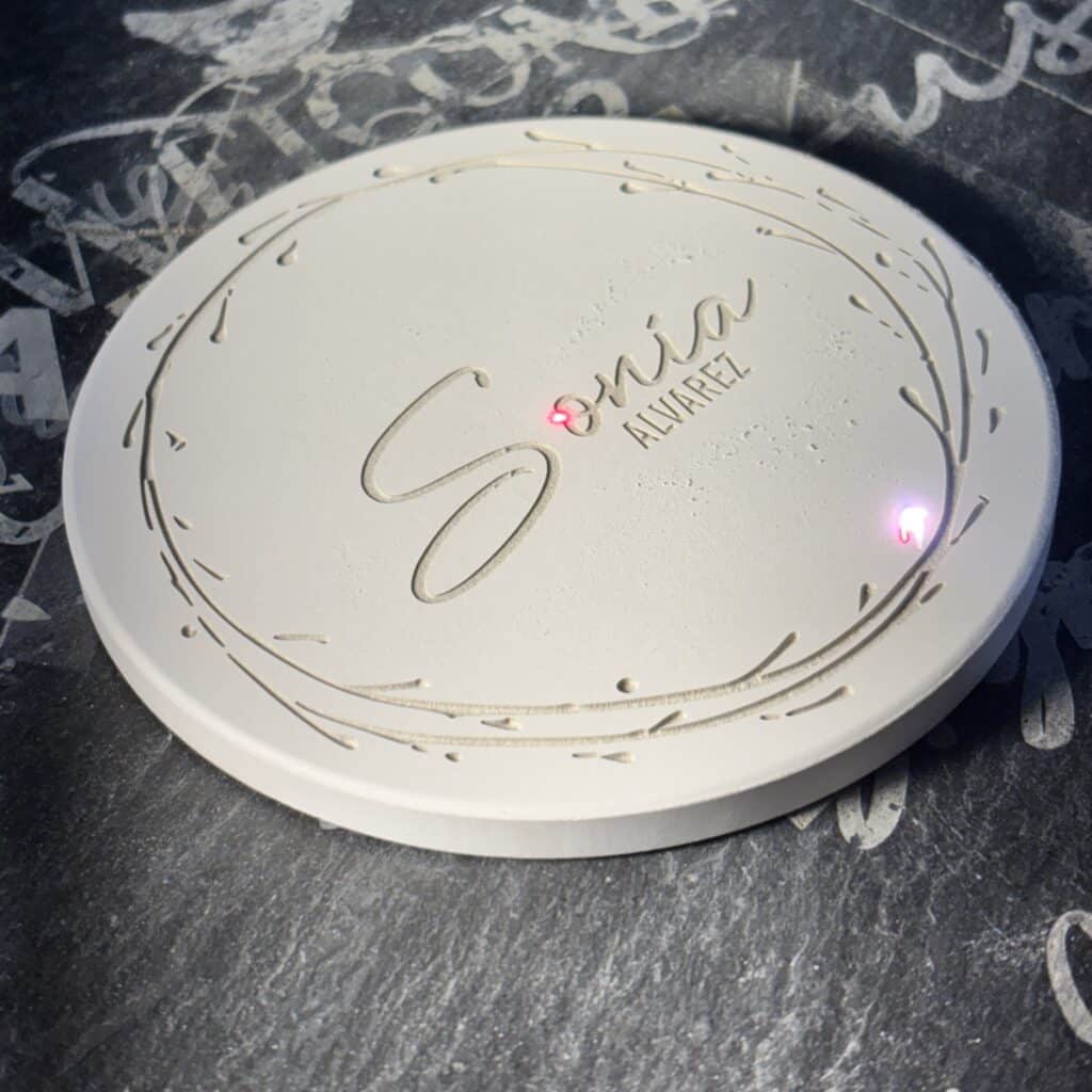 Close-up of a white decorative plate with embossed cursive script and small sauce droplets on a dark textured surface.