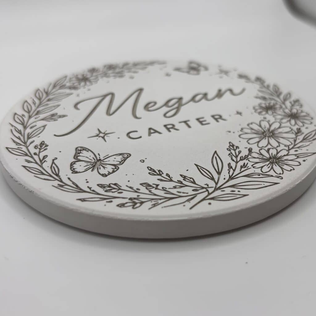 A round white coaster with floral and butterfly designs, featuring the name Megan Carter in cursive and print lettering.