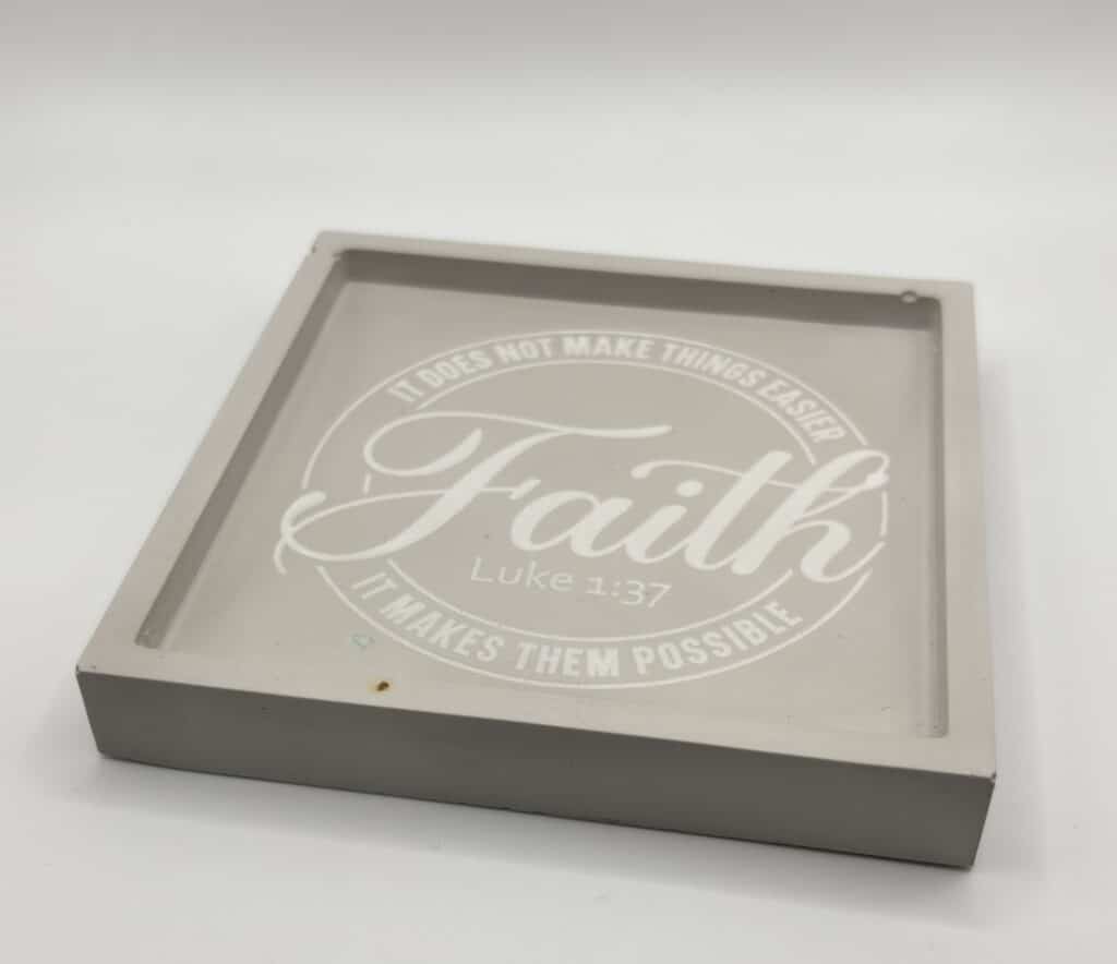 A square gray tray with the word Faith and the Bible verse Luke 1:37 printed in white, along with the phrases It does not make things easier, it makes them possible.
