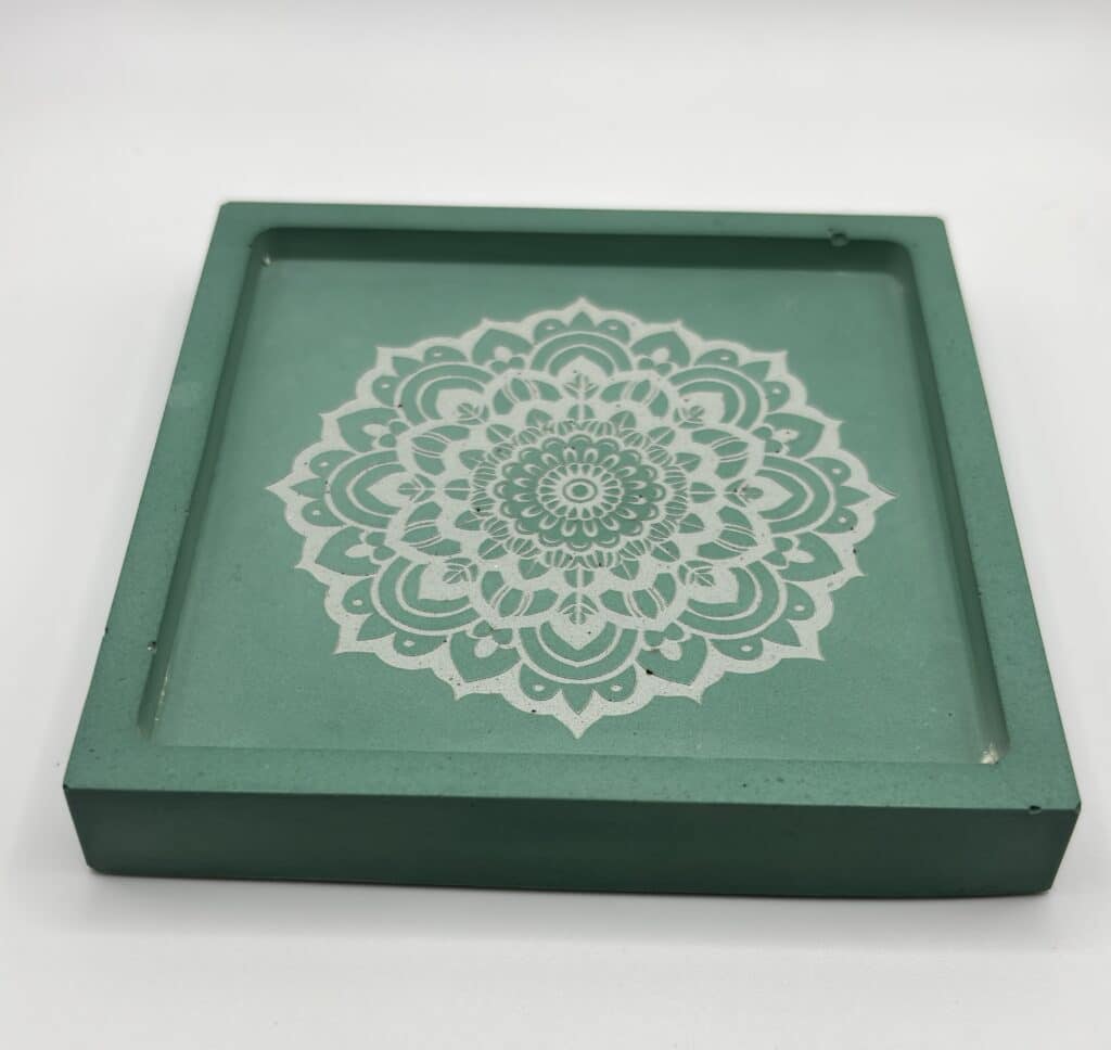 A green square coaster with a detailed white mandala pattern in the center, displayed on a plain white background.