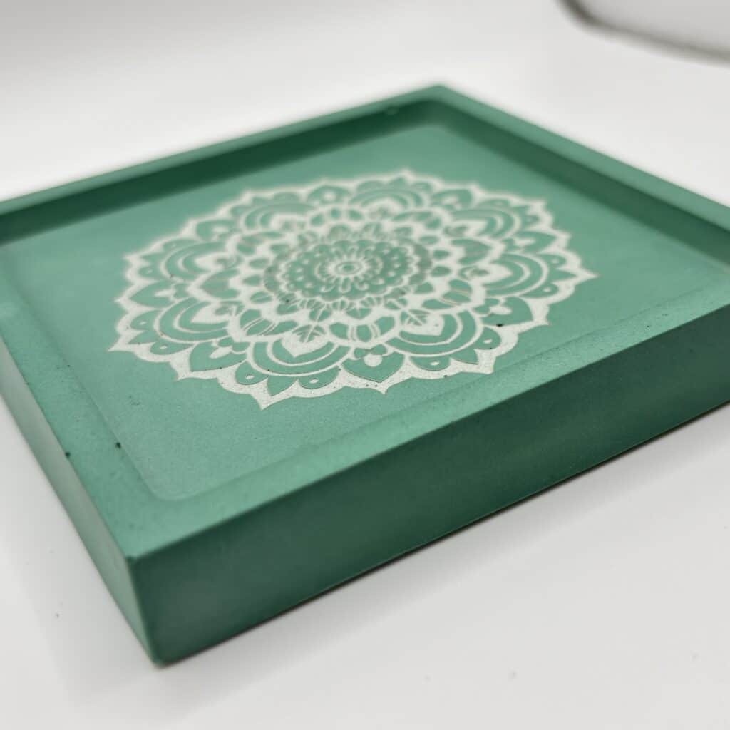 Green box lid with a white mandala pattern, photographed at an angle on a light surface