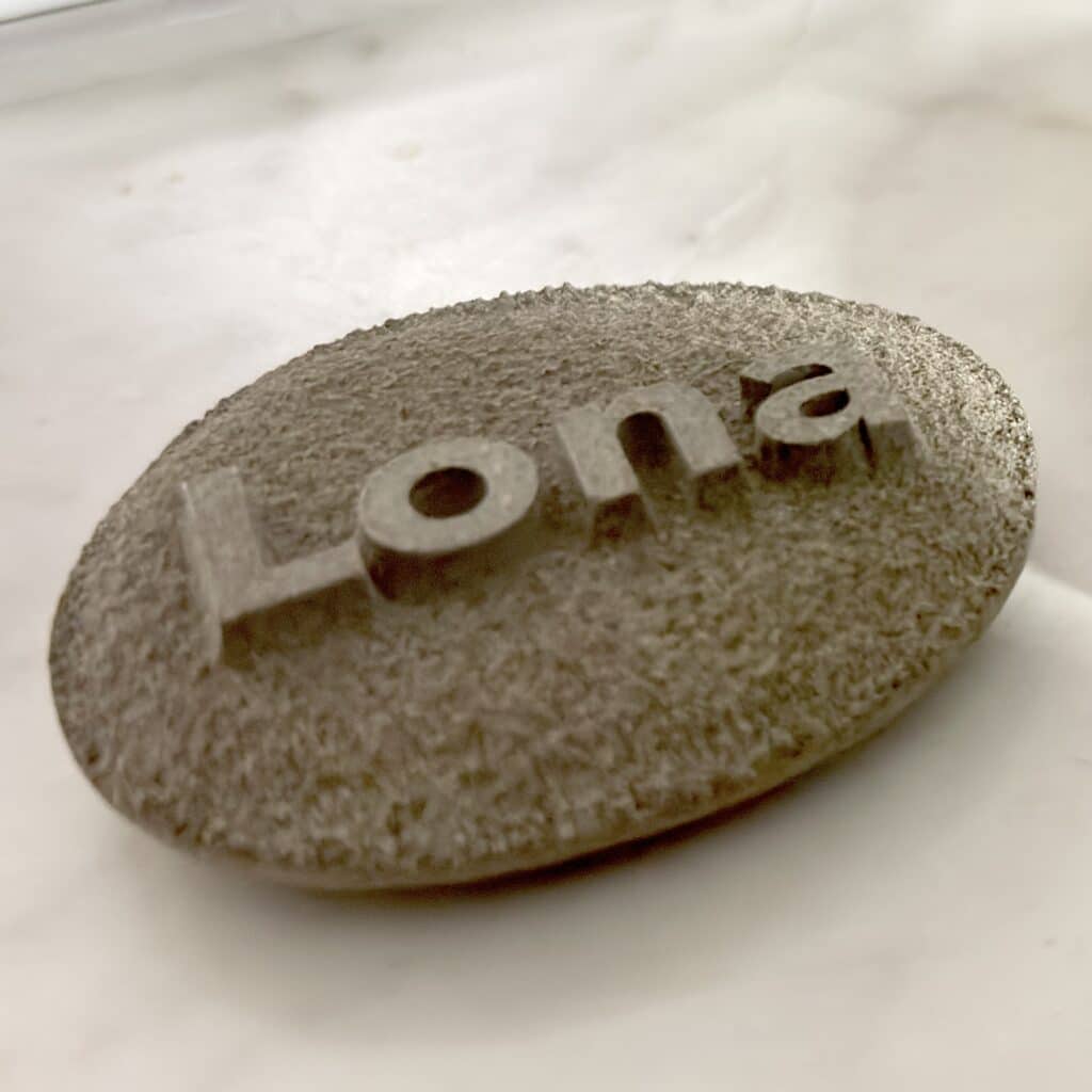 Rough textured stone sphere with metal letters partly visible against a pale, marble-like background.