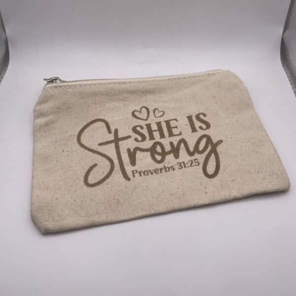 A Custom Engraved Natural Canvas Zipper Pouch in beige, featuring “She is Strong Proverbs 31:25” and two heart outlines printed in brown text on the front.