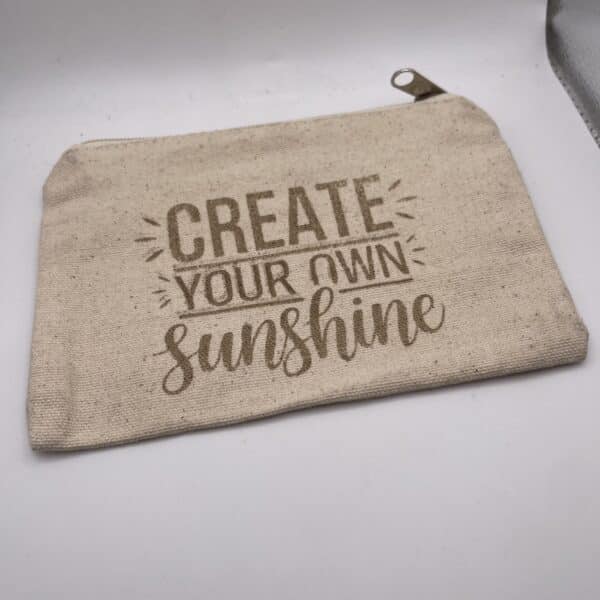 A Custom Engraved Natural Canvas Zipper Pouch in beige, featuring the phrase “CREATE YOUR OWN sunshine” in brown decorative lettering, displayed on a white surface.