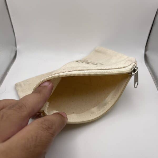 A hand holds open a Custom Engraved Natural Canvas Zipper Pouch, displaying its empty interior against a plain white background.