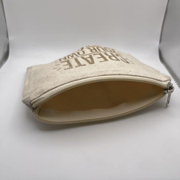 A Custom Engraved Natural Canvas Zipper Pouch in a small size and beige color is pictured unzipped and empty, with partially visible text on the front, lying on a white surface and light gray background.