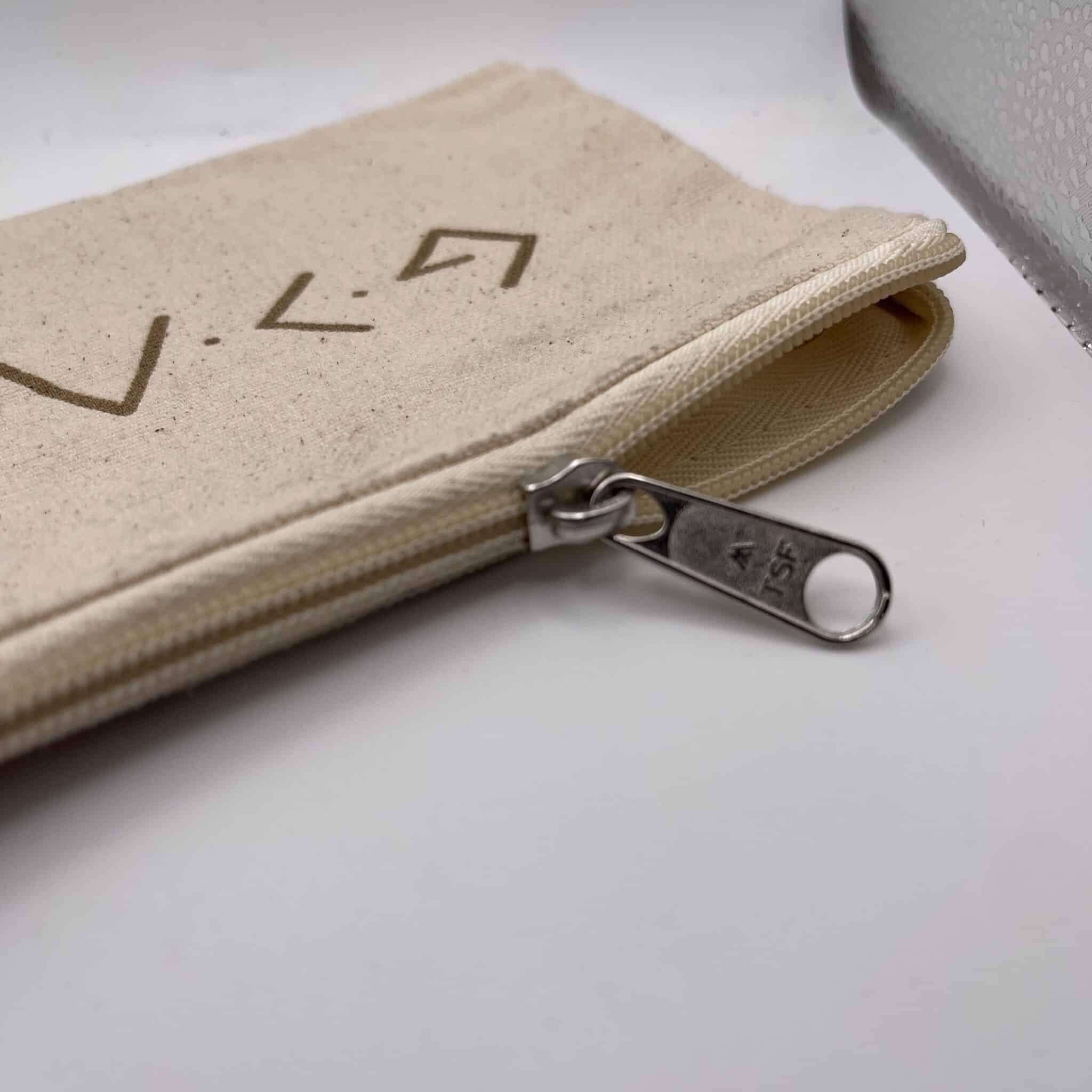 Beige fabric zip pouch on a white surface with metal scissors in the foreground