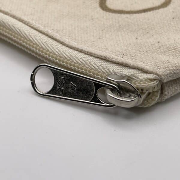 Close-up view of the silver zipper pull on the Custom Engraved Natural Canvas Zipper Pouch, showing “TSF” engraved on the metal zipper. The zipper is partially unzipped, revealing the pouch’s plain beige canvas fabric.