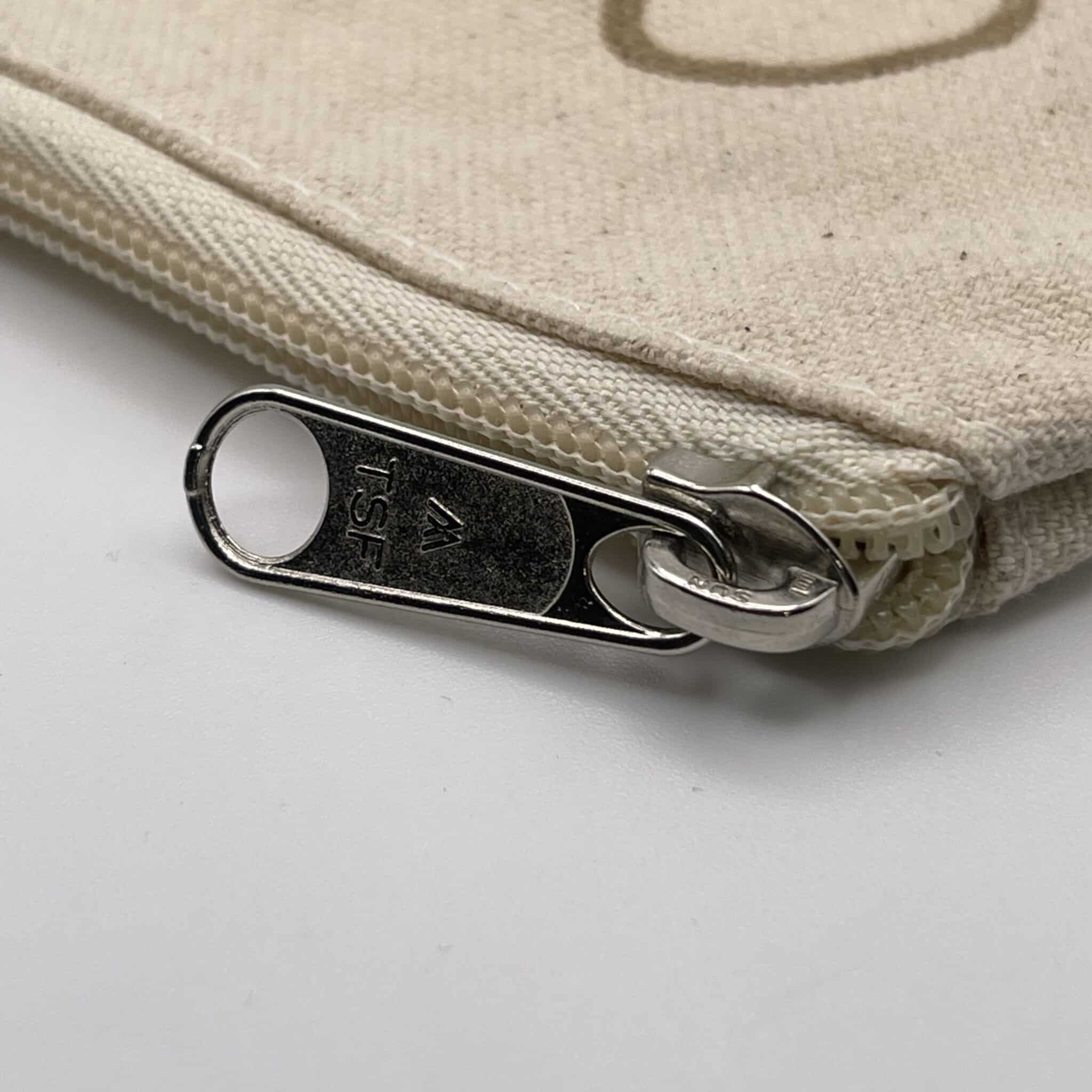 Close-up view of the silver zipper pull on the Custom Engraved Natural Canvas Zipper Pouch, showing “TSF” engraved on the metal zipper. The zipper is partially unzipped, revealing the pouch’s plain beige canvas fabric.