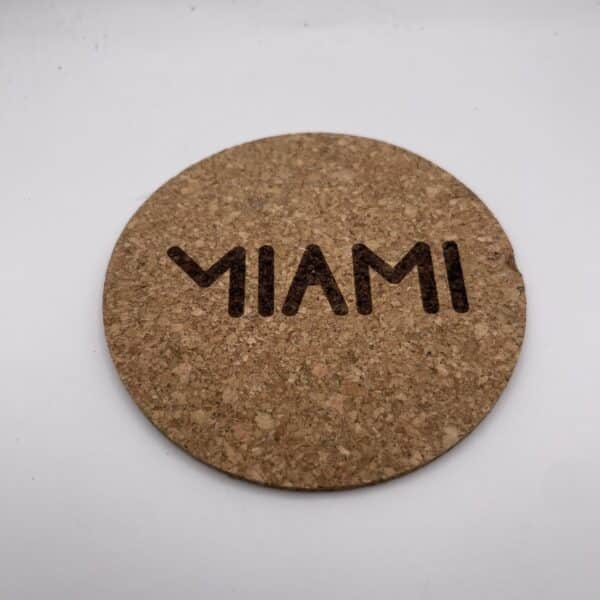 Close-up of a round cork coaster on a white background, showing a row of dark holes along its lower edge.