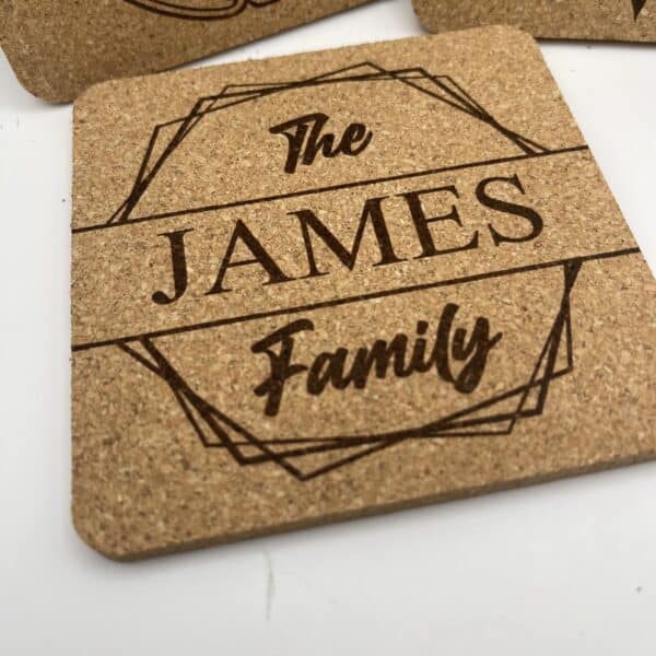 A Square 0.20″ Thick Cork Coaster engraved with “The JAMES Family” in decorative script inside a geometric border, displayed on a white background.
