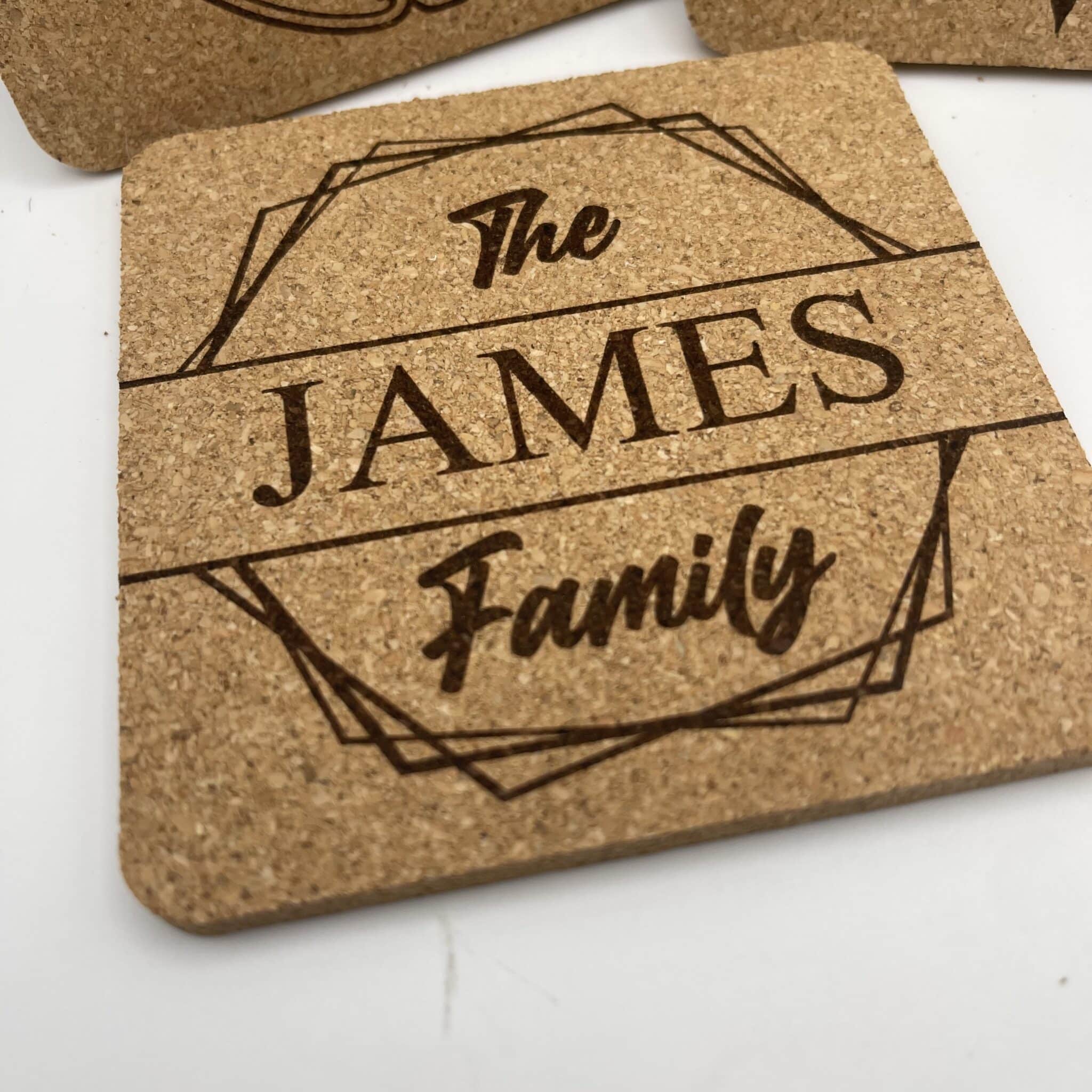 A Square 0.20″ Thick Cork Coaster engraved with “The JAMES Family” in decorative script inside a geometric border, displayed on a white background.