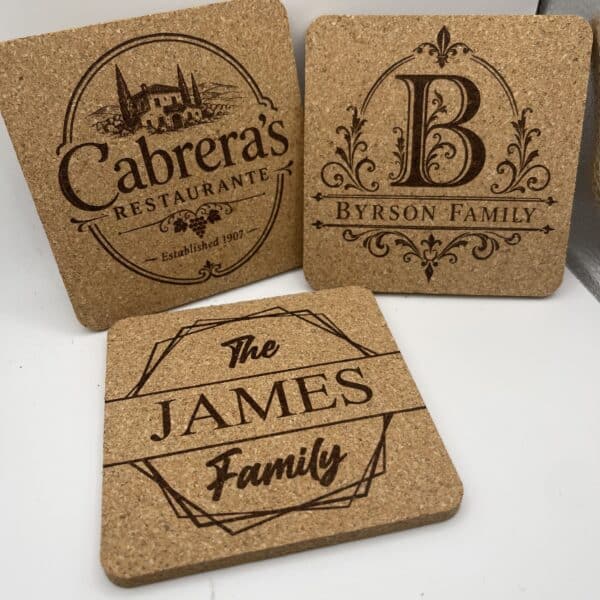 Set of three Square 0.20″ Thick Cork Coasters featuring engraved designs: Cabreras Restaurante, an ornate B Bryson Family monogram, and The James Family in bold script with decorative borders.