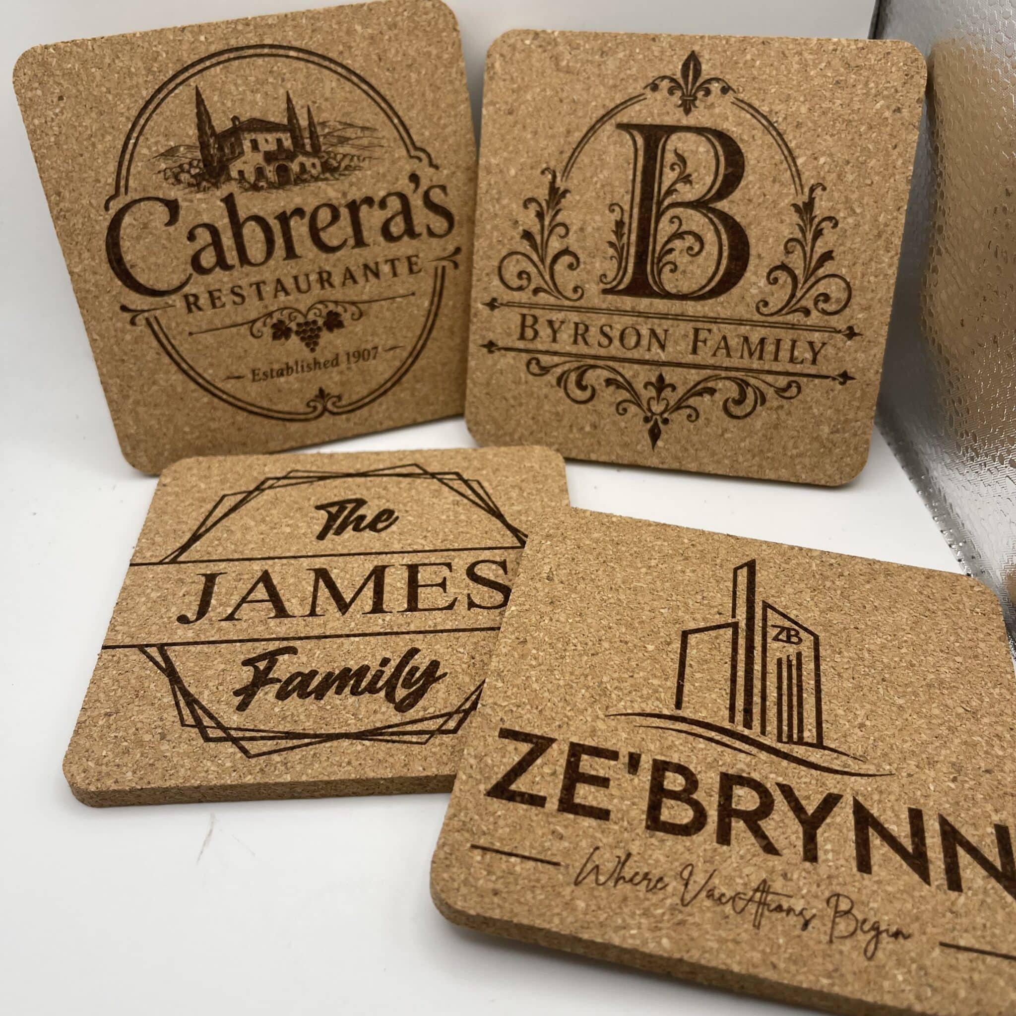 Four Square 0.20″ Thick Cork Coasters with personalized engravings—Cabreras Restaurante, B Byron Family, The James Family, and ZeBrynn Where Vacation Begins—displayed together on a white surface.