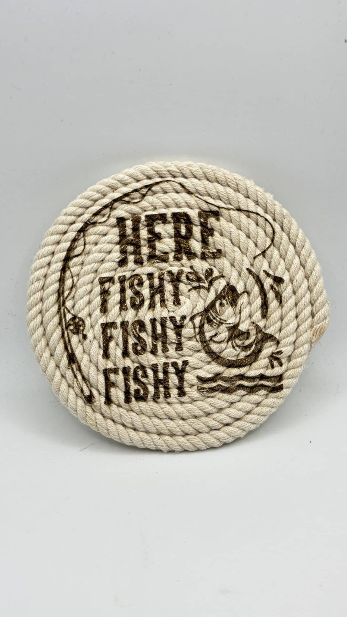 Beige circular rope badge with brown printed text reading 'FISHY' repeated and a small fish illustration.
