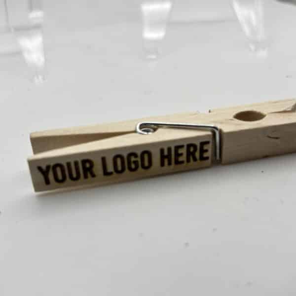 Wooden clothespin with a metal spring on a white surface, showing the placeholder text 'YOUR LOGO HERE'.