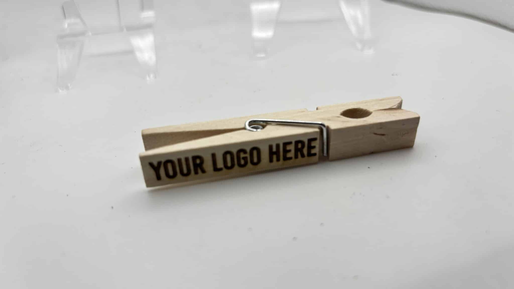 Wooden clothespin with a metal spring on a white surface, showing the placeholder text 'YOUR LOGO HERE'.